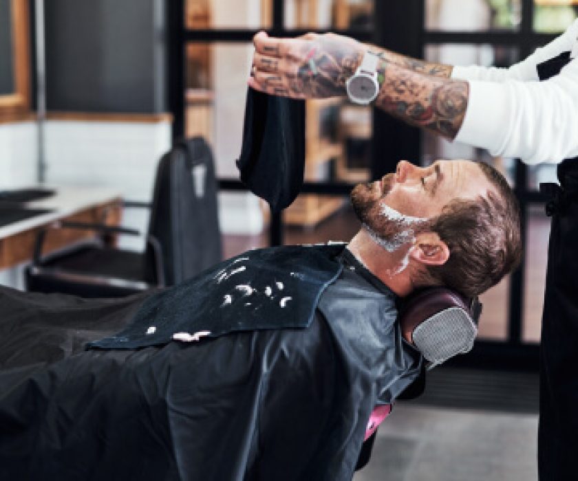 Barbier professionnel préparant un soin à la serviette chaude pour un client avec de la mousse à raser.