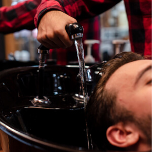 Gros plan d'un barbier lavant les cheveux d'un client dans un bac professionnel noir.