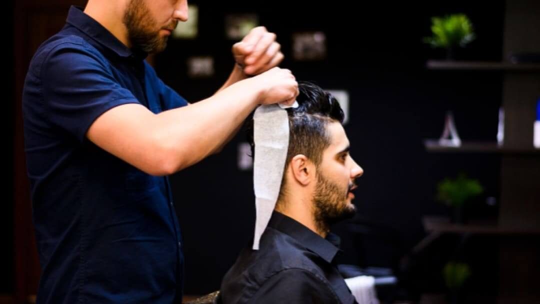 Un coiffeur professionnel coiffant avec soin les cheveux d'un homme dans un salon moderne, mettant l'accent sur un style précis et soigné.