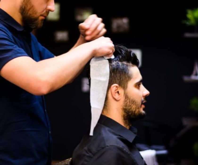 Un coiffeur professionnel coiffant avec soin les cheveux d'un homme dans un salon moderne, mettant l'accent sur un style précis et soigné.
