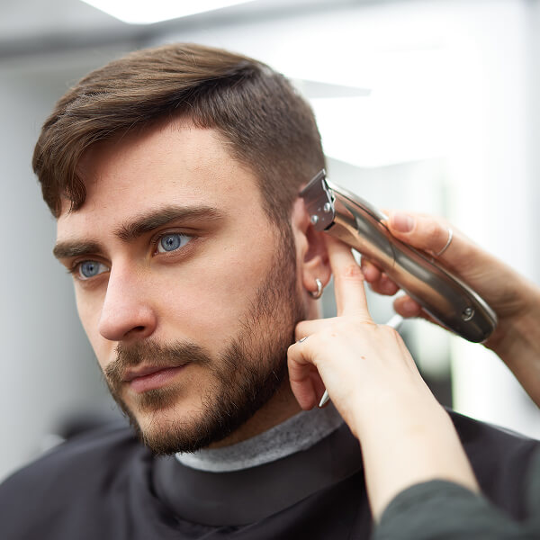 Un homme se fait couper les cheveux, illustrant les tendances capillaires prévues pour 2026.